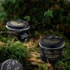 Relax Time Natural Soy Candle in a black tin container with botanical design, placed on a mossy forest floor.