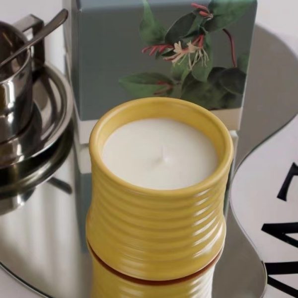 Yellow ceramic soy candle on a reflective surface with a floral box in the background